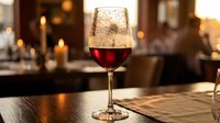 Elegant red wine glass on wooden table in upscale restaurant with warm candlelight ambiance creating sophisticated dining atmosphere for romantic evening.