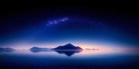 Panoramic mountain silhouette reflected in calm water under starry night sky with Milky Way galaxy arc and purple cosmic glow creating ethereal landscape.