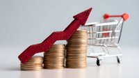 Rising stacks of gold coins with red upward arrow showing growth and shopping cart in background, representing retail sales increase and economic growth.