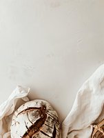 Artisanal sourdough bread loaf with rustic crust on white linen cloth, minimalist food photography composition with negative space for text placement.