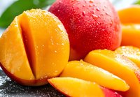 Fresh ripe mango slices with water drops and whole red mango on green leaf background, juicy tropical fruit macro photography for food design.