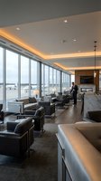 Luxury airport lounge interior with panoramic windows, comfortable seating, warm lighting and businessman waiting for departure in modern terminal space.