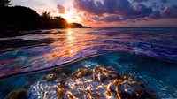 Dramatic split view of tropical sunset with vibrant sky above water and illuminated coral reef underwater, showing nature's contrast between air and sea at dusk.