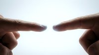 Two human index fingers pointing toward each other with a glowing light between fingertips, symbolizing connection, technology, and digital interaction.