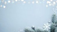 Winter holiday background with fir branches, silver ornaments and snowflakes on light blue surface with bokeh lights for festive greeting cards.