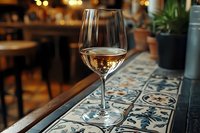 Glass of white wine on decorative tile bar counter in upscale restaurant or wine bar setting with warm ambient lighting and blurred interior background.