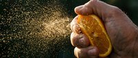 Closeup of hand squeezing fresh orange slice with juice spray against dark background, citrus fruit freshness and natural vitamin C source for healthy lifestyle and food photography.