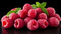Fresh ripe raspberries with green leaves isolated on black background, perfect for food packaging, menu design, and healthy eating concepts.