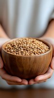 Hands holding wooden bowl filled with dried coriander seeds for cooking and seasoning in kitchen setting for culinary and food preparation concepts.