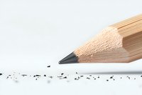 Sharp wooden pencil tip with graphite shavings scattered on white surface, macro photography showing fine detail and texture in minimalist composition.