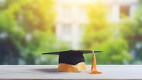 Graduation cap with gold tassel on wooden surface against blurred green background, symbolizing academic achievement and educational success in soft natural light.