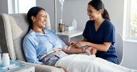 Smiling Hispanic female nurse checking blood pressure of relaxed Asian senior woman patient during home healthcare visit in bright living room.
