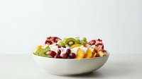 Fresh fruit salad with kiwi, pomegranate, grapes and citrus in white bowl on clean background for healthy eating and nutrition concepts.