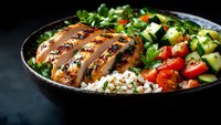 Grilled chicken breast with fresh garden salad and brown rice in dark bowl on black background. Healthy protein-rich meal with vegetables.