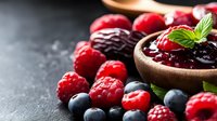 Fresh mixed berries with raspberry jam in wooden bowl on dark slate background for healthy breakfast and dessert recipes.