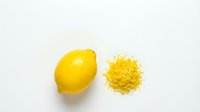 Fresh whole lemon with grated zest pile on white background, top view. Citrus ingredient for cooking, baking, and flavoring recipes.