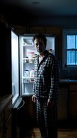 Middle-aged Caucasian man in plaid pajamas standing by open refrigerator in dark kitchen during late night snacking or insomnia episode for lifestyle concepts.