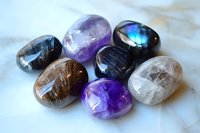 Polished gemstones and crystals including amethyst, labradorite, and moonstone arranged on white marble surface showing natural mineral textures and iridescent colors.