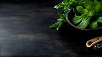 Fresh green mint leaves in rustic bowl on dark moody background with copy space. Raw organic herbs for cooking, cocktails and tea preparation.