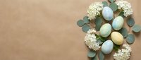 Pastel Easter eggs with white flowers and eucalyptus leaves arranged on beige background for spring holiday decorations and greeting cards.