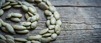 Green cardamom pods arranged in spiral pattern on rustic wooden surface for culinary and spice photography applications.