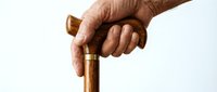Elderly hand gripping wooden walking cane against white background showing aging support mobility assistance healthcare concept for senior independence.