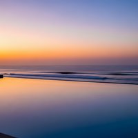 Serene ocean beach at sunset with purple and orange sky reflecting on wet sand and gentle waves creating peaceful coastal atmosphere.