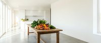 Modern minimalist kitchen interior with wooden dining table displaying fresh vegetables and herbs for healthy cooking and meal preparation.