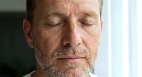 Peaceful middle-aged Caucasian man with closed eyes and gray beard in serene meditation pose, expressing mindfulness and inner calm for wellness content.