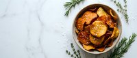Golden crispy potato chips with fresh rosemary and thyme herbs in rustic wooden bowl on white marble background for cooking and snack concepts.