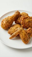 Crispy fried chicken drumsticks and wings with golden-brown seasoned coating served on white plate for food photography, restaurant menus, and culinary content.
