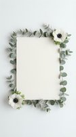 Blank paper card surrounded by eucalyptus branches and white anemone flowers on neutral background for wedding invitations and stationery design.