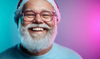 Cheerful senior Caucasian man with white beard and glasses wearing Santa hat smiling broadly against colorful gradient background. Holiday portrait concept.