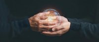 Elderly hands gently holding glowing crystal ball with mystical light emanating from within against dark background for fortune telling concepts.