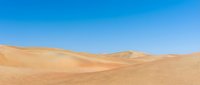 Vast desert landscape with rolling sand dunes under clear blue sky, suitable for travel, nature, and background design projects.