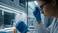 Female scientist in protective eyewear and blue gloves conducting laboratory research with pipette and test tubes in modern scientific facility.