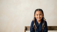 Young girl with braided hair wearing denim shirt, smiling at camera against neutral background. Portrait suitable for educational materials, diversity campaigns, and family-oriented designs.