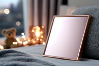 Rose gold metallic frame on cozy gray sofa with soft bokeh lights and teddy bear in background, creating warm atmospheric home interior setting.