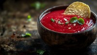 Fresh homemade beetroot soup garnished with microgreens and crispy tortilla chip served in rustic wooden bowl on dark background with copy space.