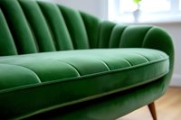 Luxurious emerald green velvet sofa with channel tufting and curved shell back design on wooden legs against bright interior background. Modern furniture piece.