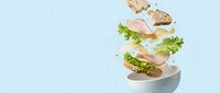 Flying sandwich ingredients with ham, lettuce and bread slices falling into white bowl on light blue background for food advertising and menu design.
