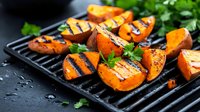 Grilled sweet potato slices with char marks on cast iron grill pan, garnished with fresh herbs and spices for healthy vegetarian meal.
