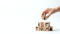 Hand placing wooden cube with lightbulb icon completing business strategy concept with growth symbols on white background for presentations.