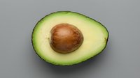 Fresh ripe avocado half with pit on gray background. Healthy organic fruit for cooking, nutrition and diet concepts. Natural food ingredient isolated.