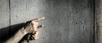 Hand pointing finger gesture against concrete wall background with dramatic lighting and shadow effects for presentations and advertising concepts.