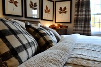 Cozy bedroom interior with plaid pillows and white quilted bedding, framed botanical prints on wall create warm autumn atmosphere for home decor styling.