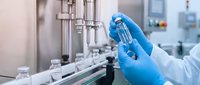 Scientist in blue gloves holding test tube in modern pharmaceutical laboratory with automated equipment. Medical research and drug development concept.