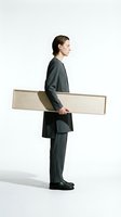 Young professional man in dark gray business suit carrying wooden plank, isolated on white background for corporate and construction industry concepts.
