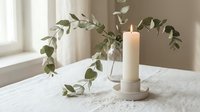 Minimalist home decor with eucalyptus branch in glass vase and lit candle on marble table creating serene atmosphere for relaxation and wellness.