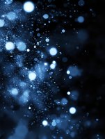 Magical blue bokeh lights and sparkles on dark background create dreamy atmosphere with glowing particles and blurred circles for festive designs.